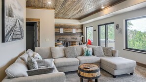 A modern living room with a large sectional sofa, a wooden ceiling, and a view of the outdoors through large windows. - Views for Days, New Cabin Near Terry Peak Ski Area w/ Hot Tub and Large Deck! (Lead)