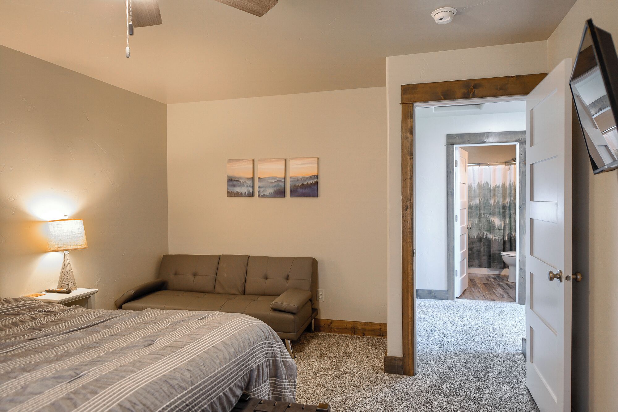 A bedroom with a bed, a sofa, a lamp, and a door leading to a bathroom.