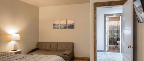 A bedroom with a bed, a sofa, a lamp, and a door leading to a bathroom.