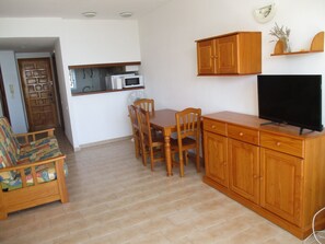 A compact living space with a dining area, a kitchenette, a television, and a sofa.