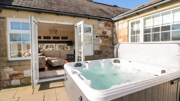 Une construction en pierre dotée d’un jacuzzi, d’une terrasse en bois et d’une cheminée en pierre.