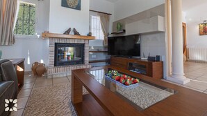 A living room with a fireplace, TV, and a coffee table with fruit. - Villa AURORA by Abahana Villas (Benissa)