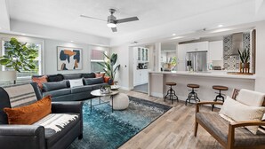 A modern living room with a sofa, coffee table, and bar stools. There is a kitchen area with a refrigerator and a sink. - Beautiful Tropical Retreat Near Fort Lauderdale Beach, Las Olas & Top Attractions (Fort Lauderdale)