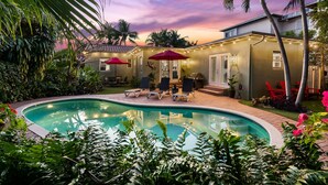 A pool area with lounge chairs and umbrellas, surrounded by lush greenery and a sunset sky. - Beautiful Tropical Retreat Near Fort Lauderdale Beach, Las Olas & Top Attractions (Fort Lauderdale)
