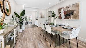A modern dining area with a long table, white chairs, and a large abstract painting on the wall. - Beautiful Tropical Retreat Near Fort Lauderdale Beach, Las Olas & Top Attractions (Fort Lauderdale)