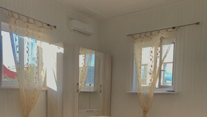 Een slaapkamer met een groot bed, twee ramen met gordijnen, een airconditioning en een deur.