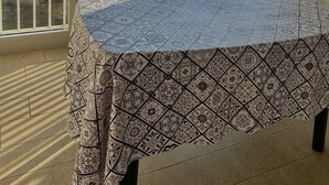 Een balkon met een tafel, gedekt met een tafelkleed met een patroon, een stoel, en uitzicht op een brug en bomen.