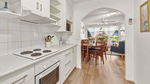 Une cuisine moderne avec des meubles blancs, un coin repas avec des chaises en bois et, à travers une arche, une vue sur un balcon.