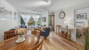 Un vaste espace de vie comprenant une table à manger, un ventilateur de plafond et une grande fenêtre agrémentée de rideaux légers.