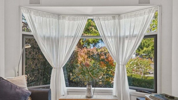 Une pièce dotée d’une baie vitrée, d’une petite table sur laquelle est posé un vase, et qui offre une vue sur les arbres à l’extérieur.
