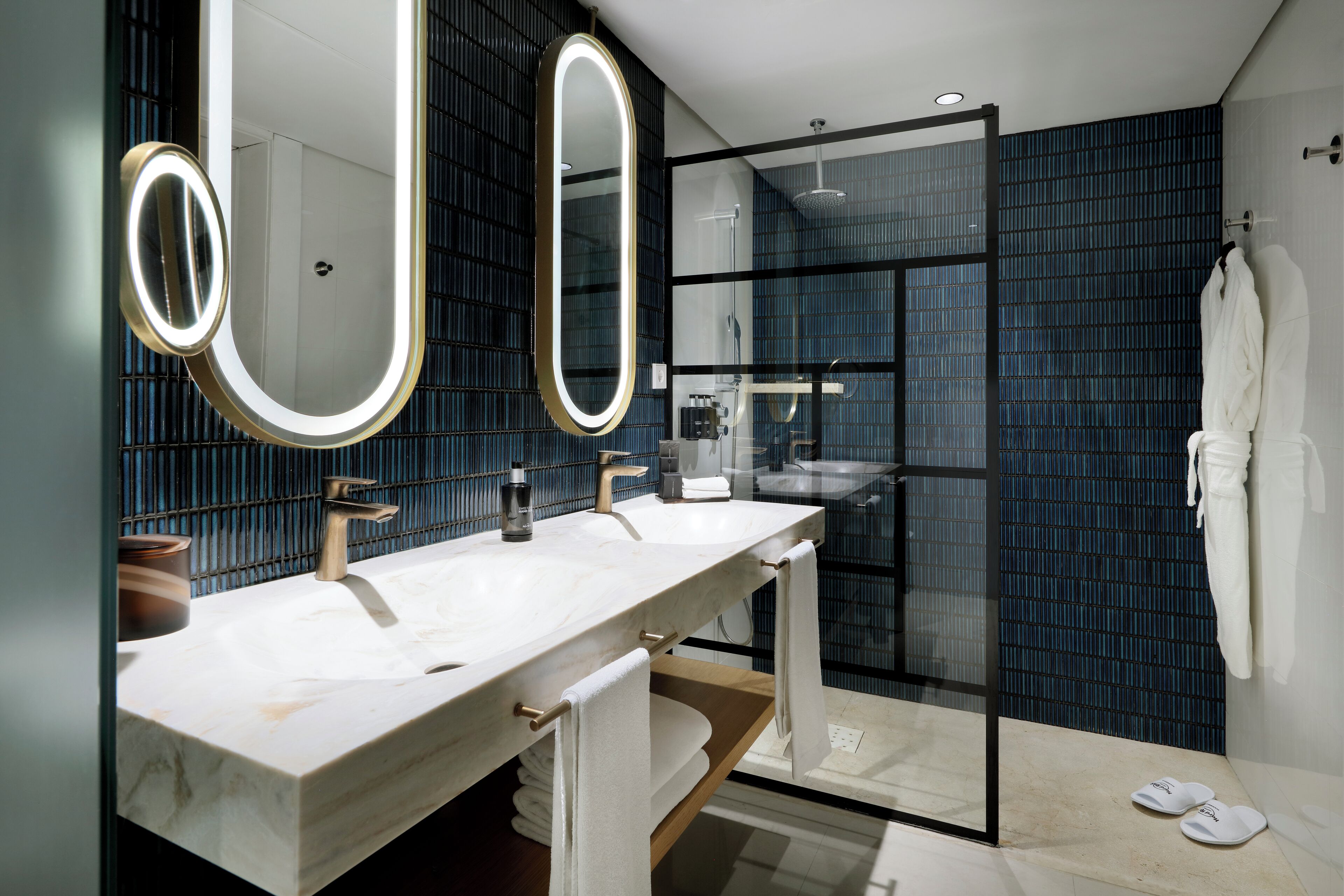 A modern bathroom with two sinks, a glass shower enclosure, and a large mirror with integrated lighting.