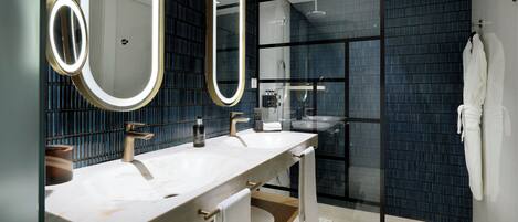 A modern bathroom with two sinks, a glass shower enclosure, and a large mirror with integrated lighting.