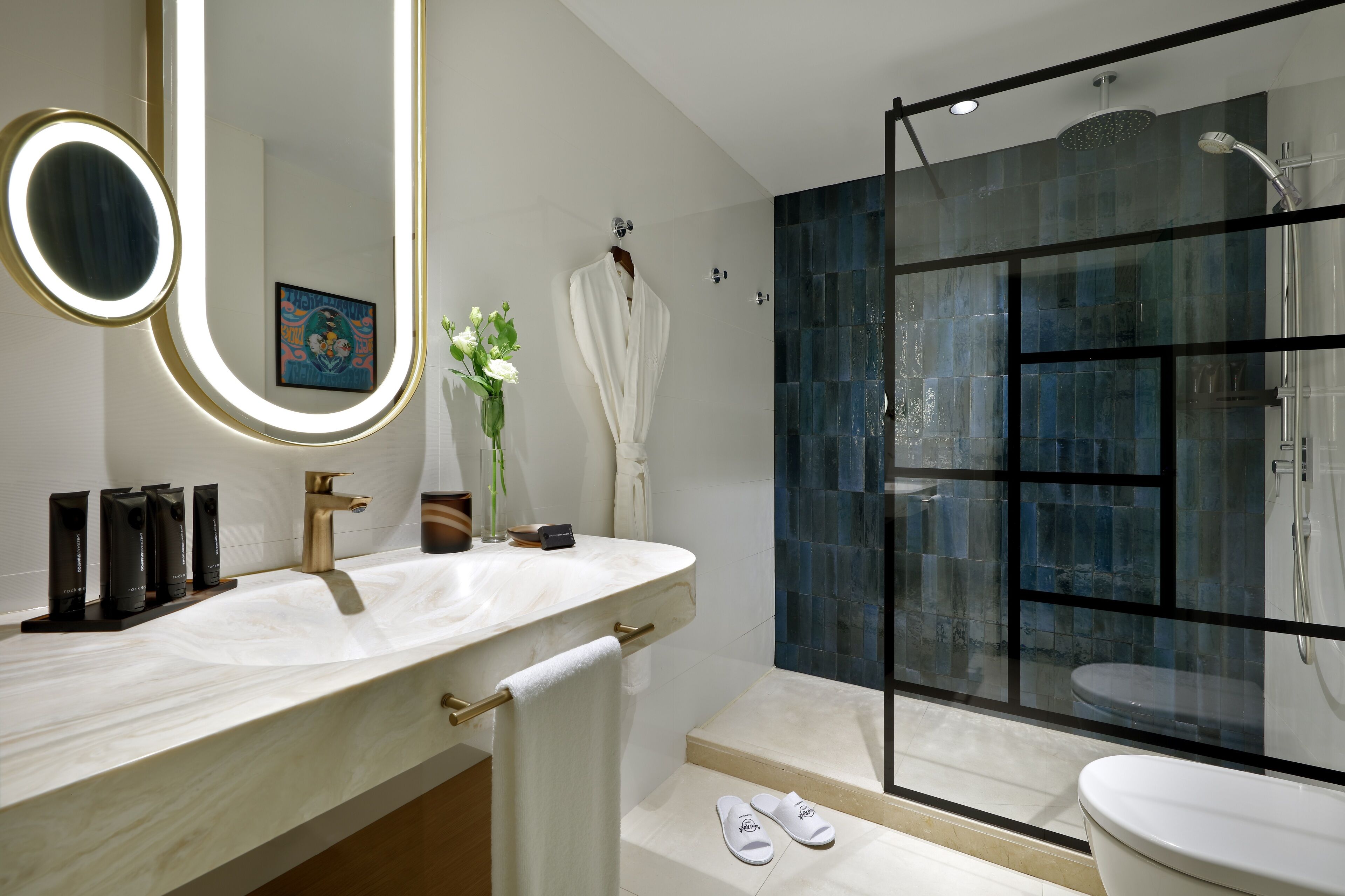 A modern bathroom with a marble sink, a glass-enclosed shower, and a large mirror with a gold frame.