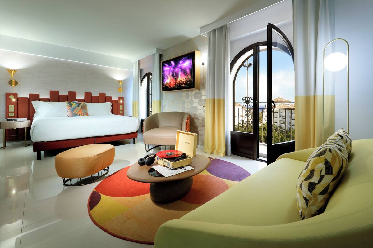 Una habitación de hotel con cama, sofá, sillón, mesa de centro y televisión.