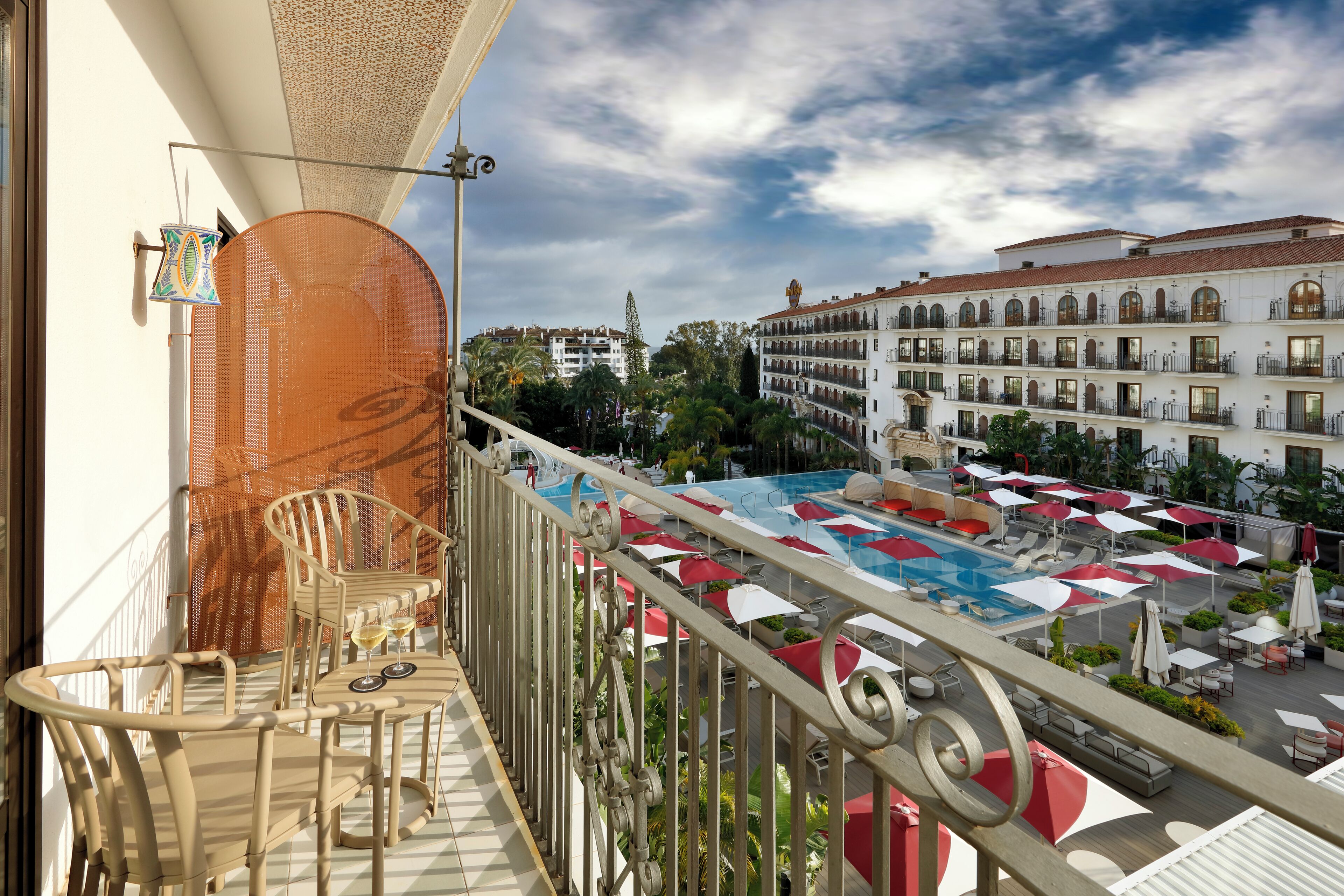 A balcony with a pool area, outdoor seating, and a view of a building with multiple balconies.