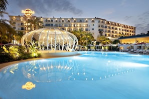 A hotel with a swimming pool, a large dome structure, and a well-lit building facade.