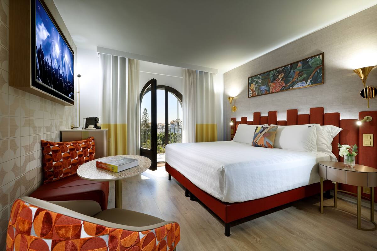 Habitación de hotel con una cama grande, un escritorio, una silla, un televisor y un cuadro en la pared.