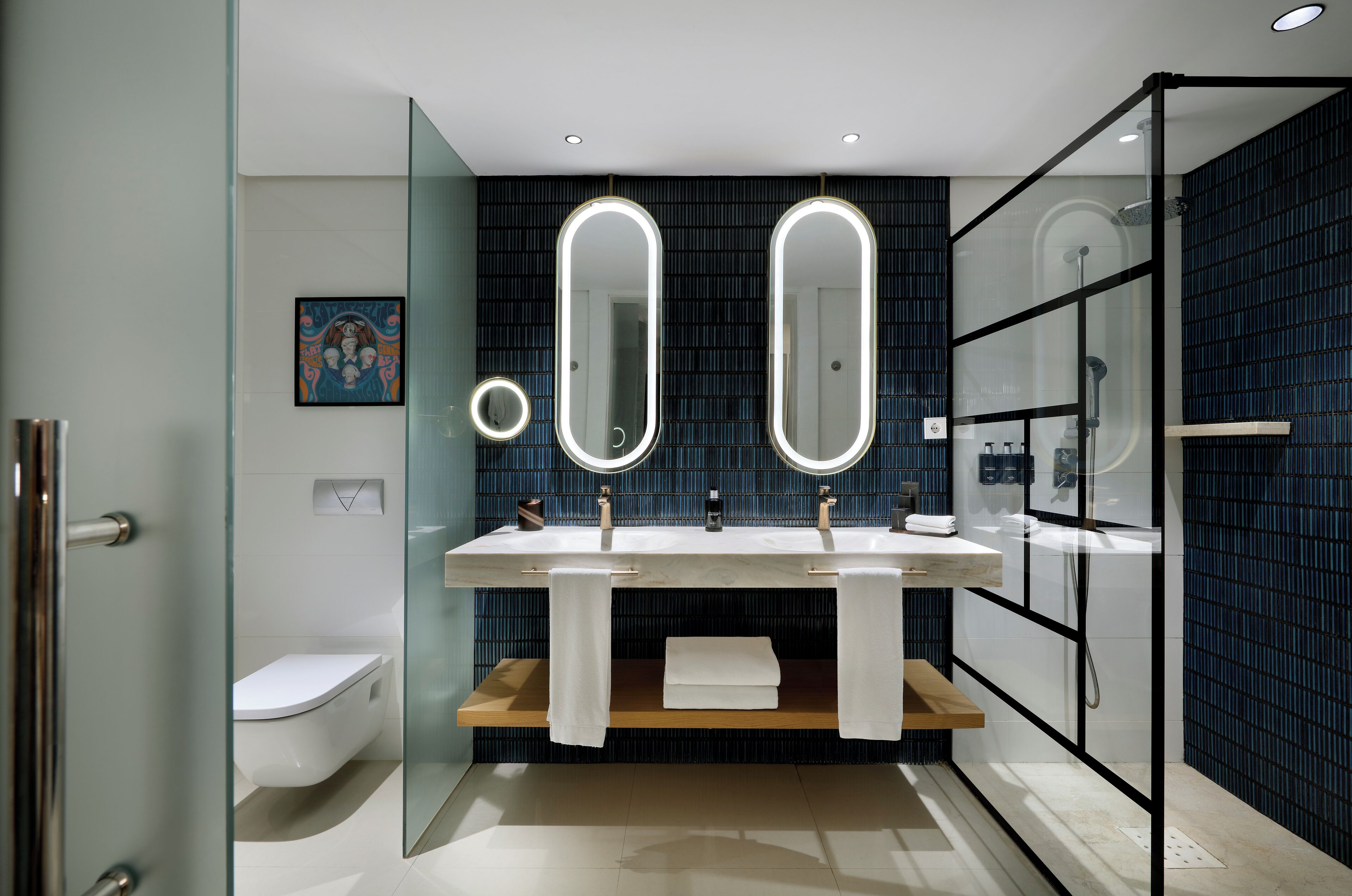 A modern bathroom with a glass shower enclosure, a white toilet, and a double sink with illuminated mirrors.