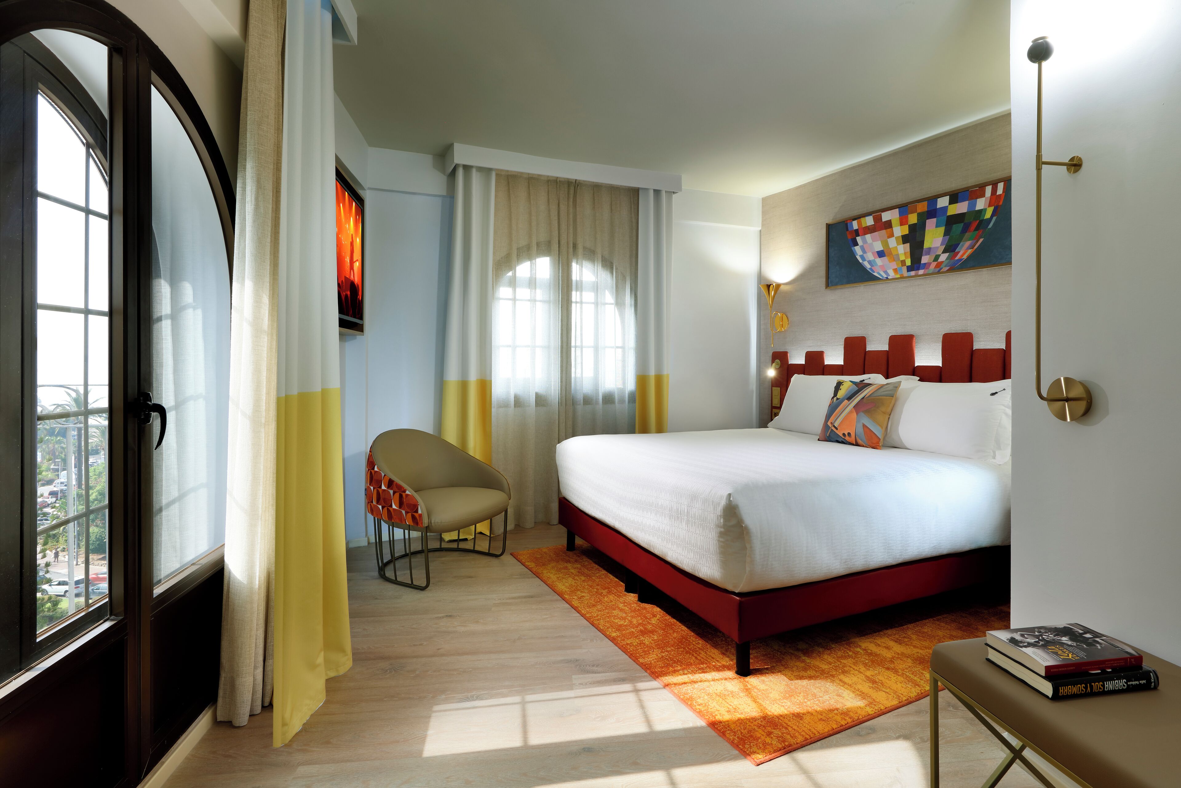 Una habitación de hotel con una cama, una silla, un ventanal y un cuadro en la pared.