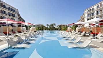 A swimming pool with lounge chairs and umbrellas, surrounded by a hotel with balconies and a clear sky.