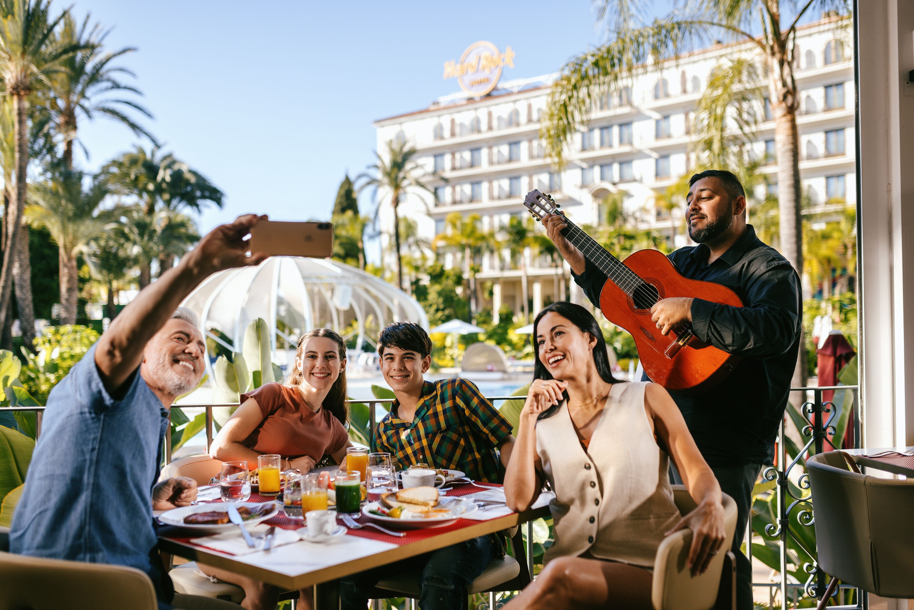 Un grupo de personas cenando al aire libre con vistas a un hotel y palmeras.