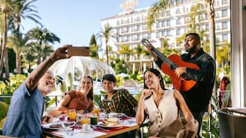 Un grupo de personas cenando al aire libre con vistas a un hotel y palmeras.