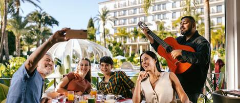A group of people dining outdoors with a view of a hotel and palm trees.
