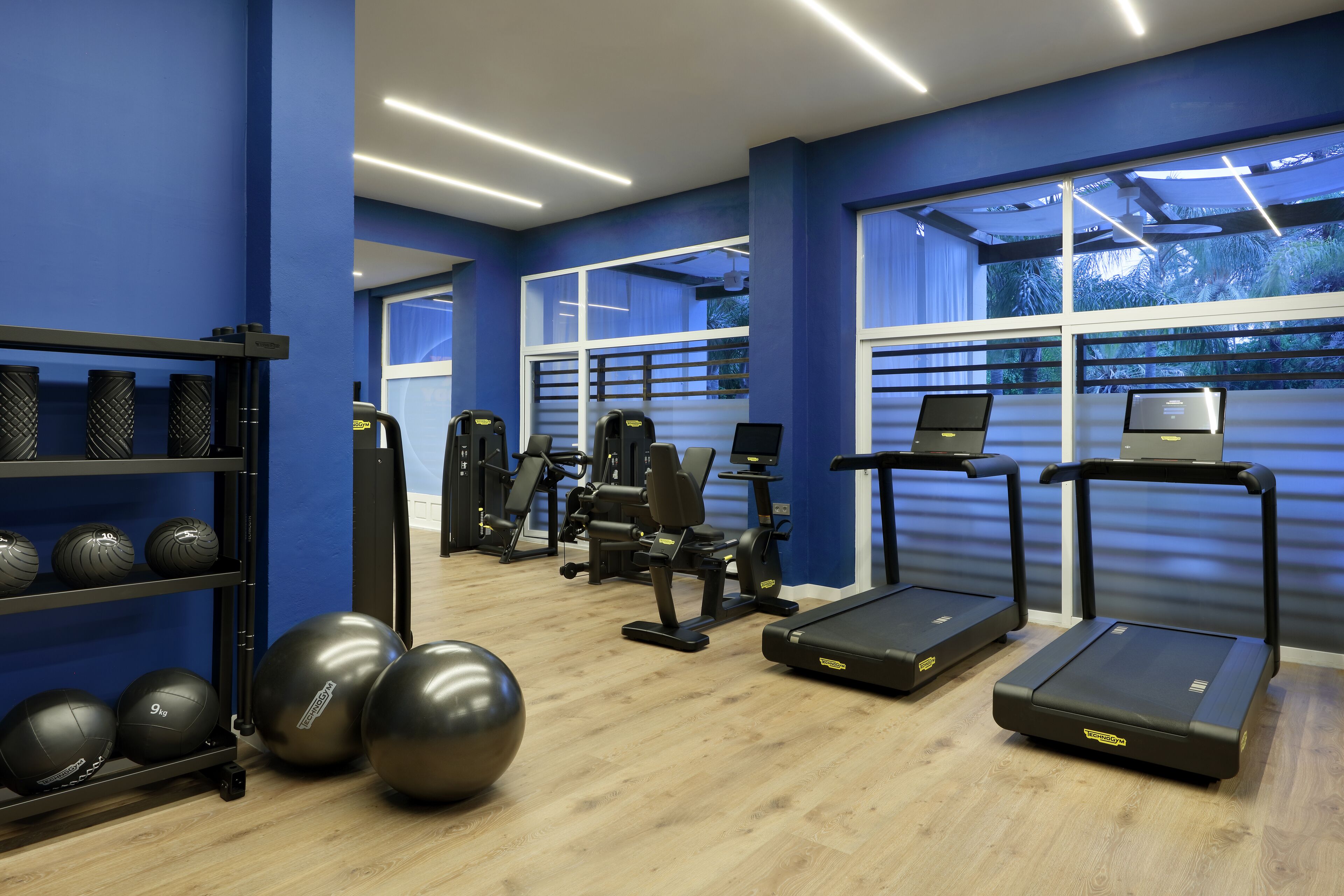 Un gimnasio con equipo de ejercicio, una cinta de correr y un ordenador portátil instalado en la pared.