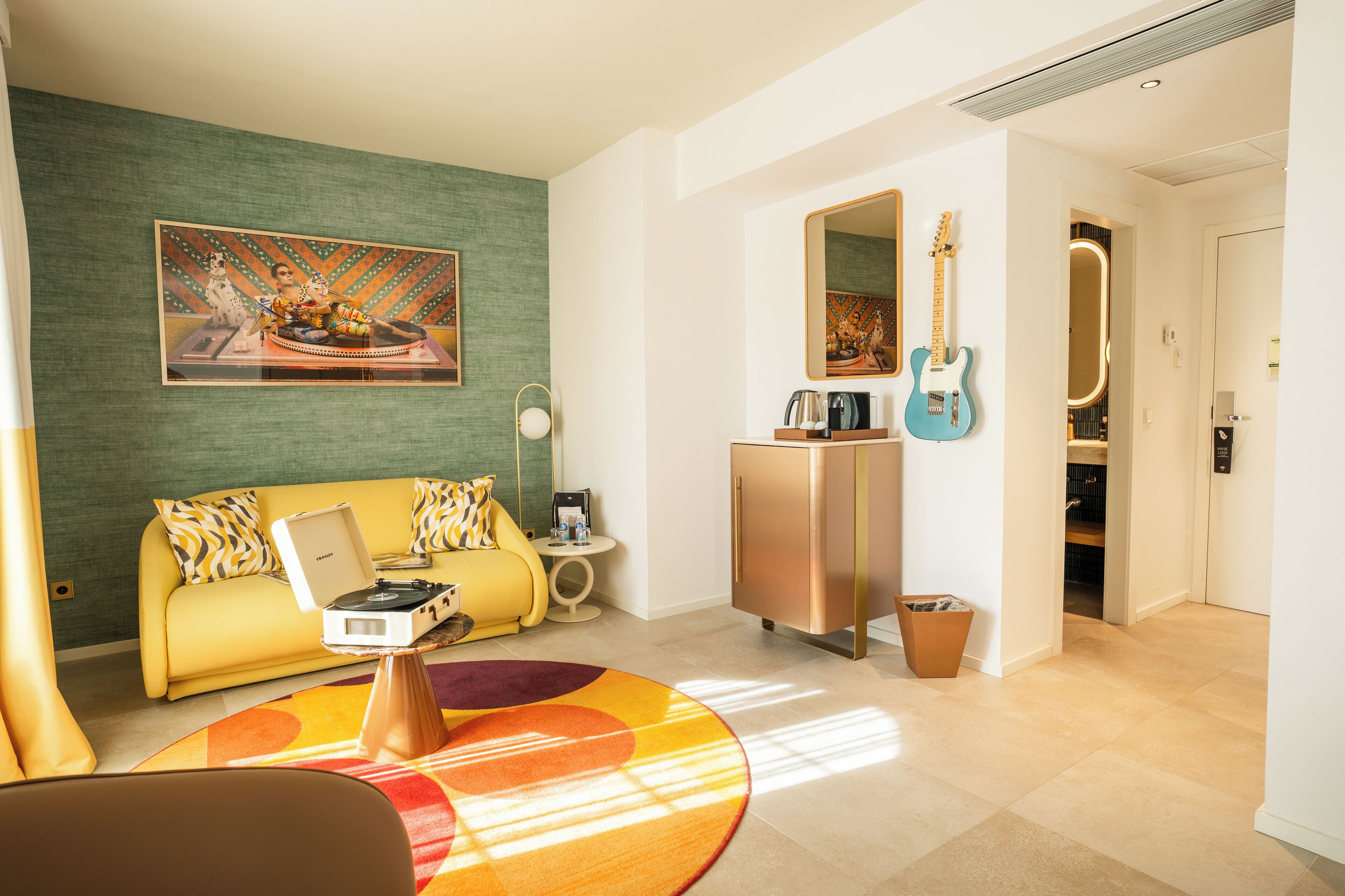 Una sala de estar moderna con un sofá amarillo, una mesa de centro, un cuadro, una guitarra y un refrigerador.