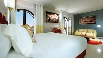 Une chambre d’hôtel avec un grand lit, un canapé et une table à manger. Il y a deux tableaux accrochés aux murs et une fenêtre avec des rideaux.