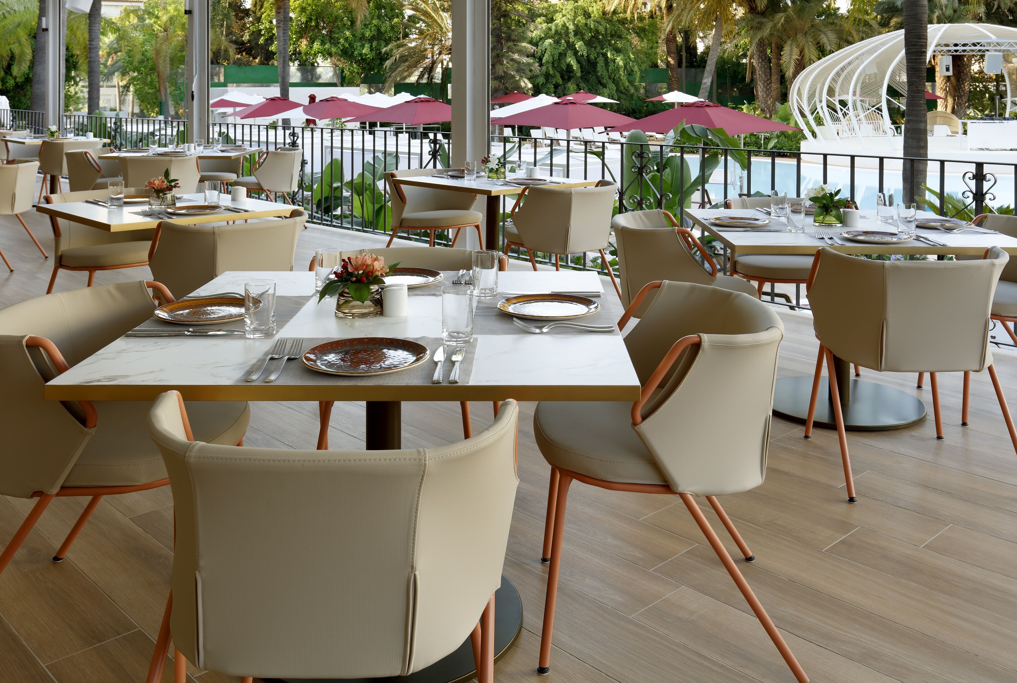 An outdoor dining area with tables set for two, surrounded by chairs with metal legs.
