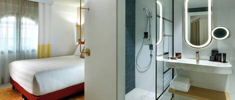 A hotel room with a bed, a bathroom with a shower, a mirror, and a shelf with toiletries.