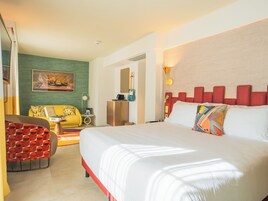 A hotel room with a large bed, a yellow sofa, a small table with a lamp, and a painting on the wall.