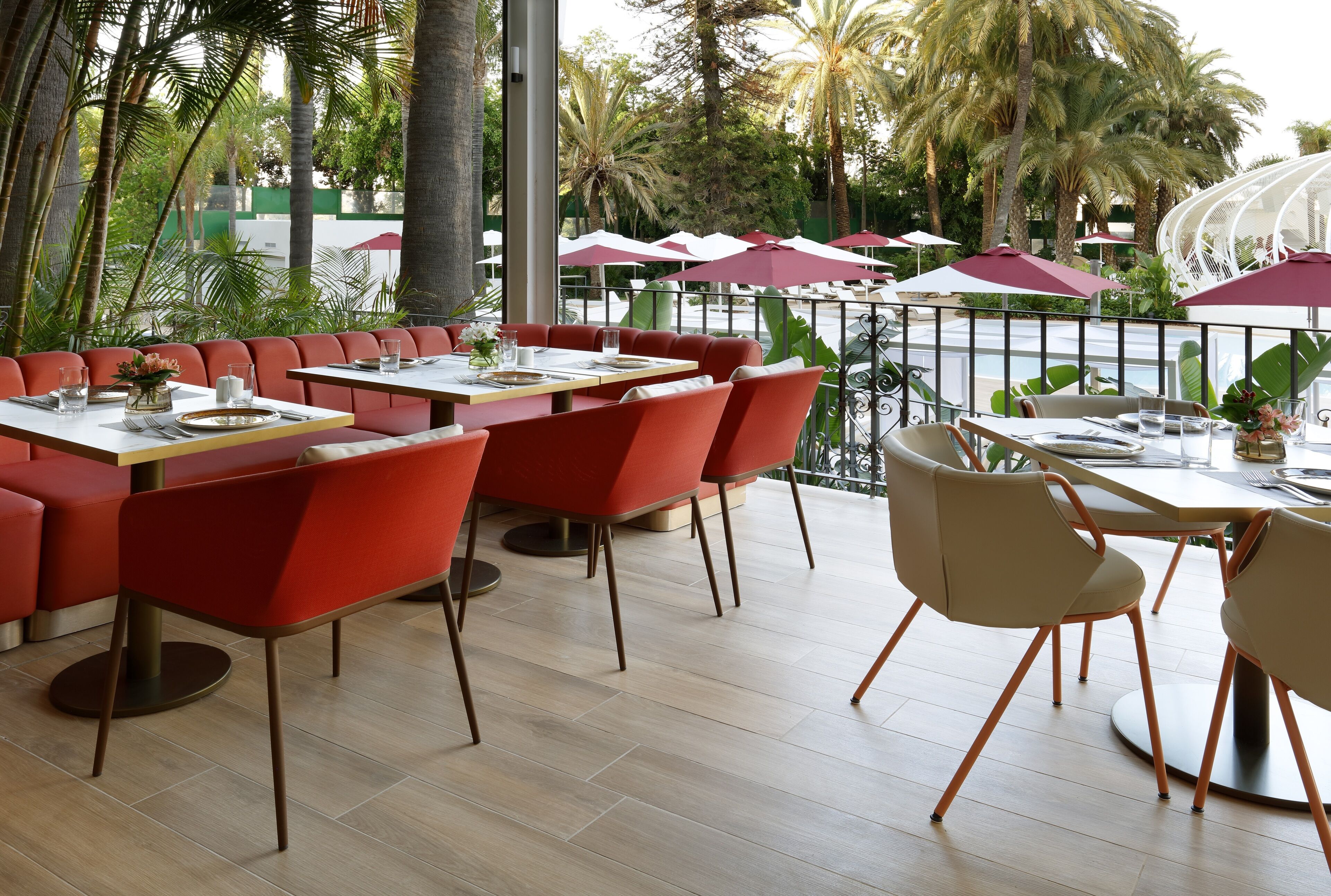 Un espace extérieur aménagé pour les repas, avec des chaises, des tables et des parasols aux couleurs rouge et beige.