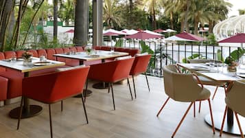 Un espace extérieur aménagé pour les repas, avec des chaises, des tables et des parasols aux couleurs rouge et beige.