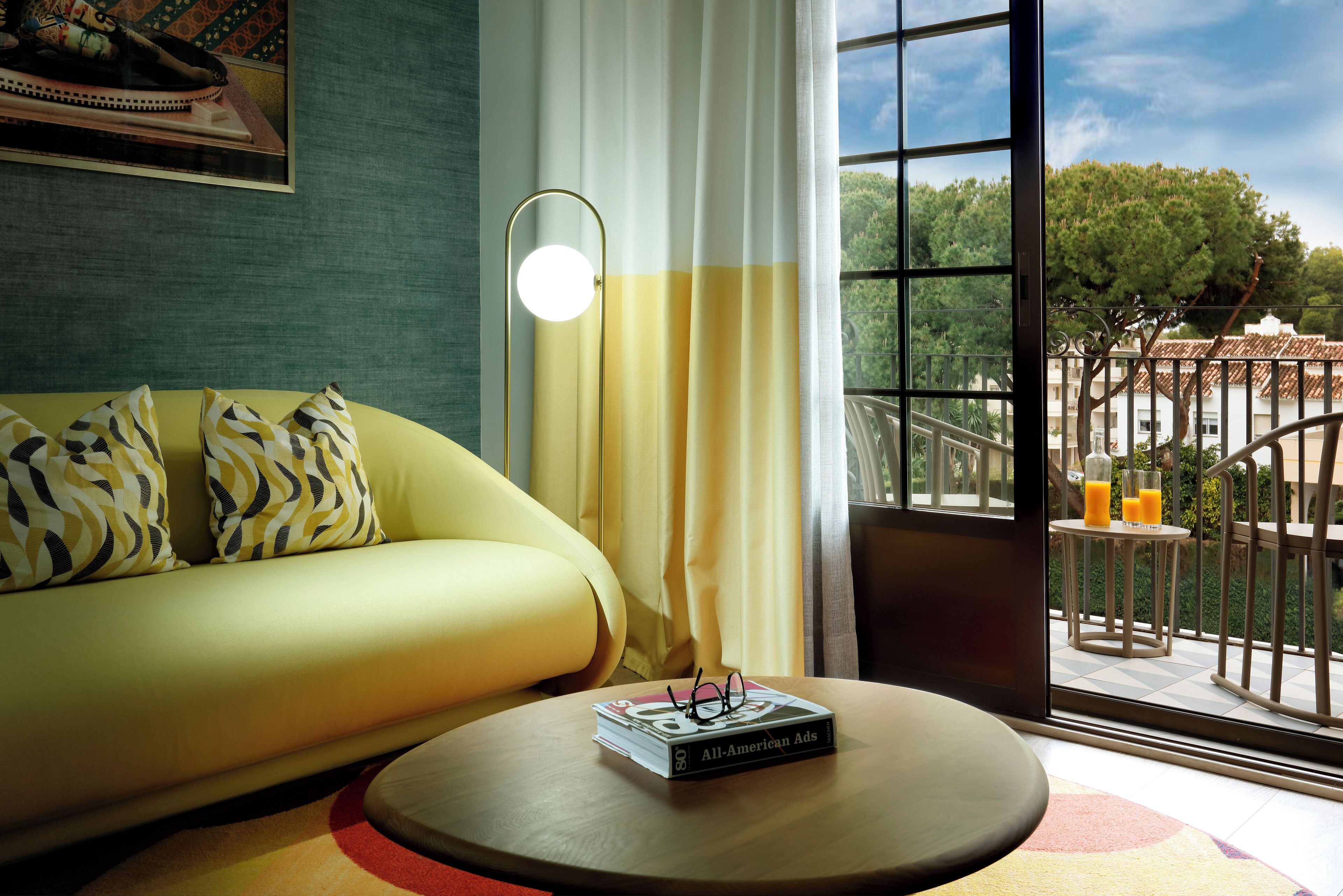 Un salon moderne avec un canapé, une table basse ronde et une vue sur un balcon doté d’une balustrade.
