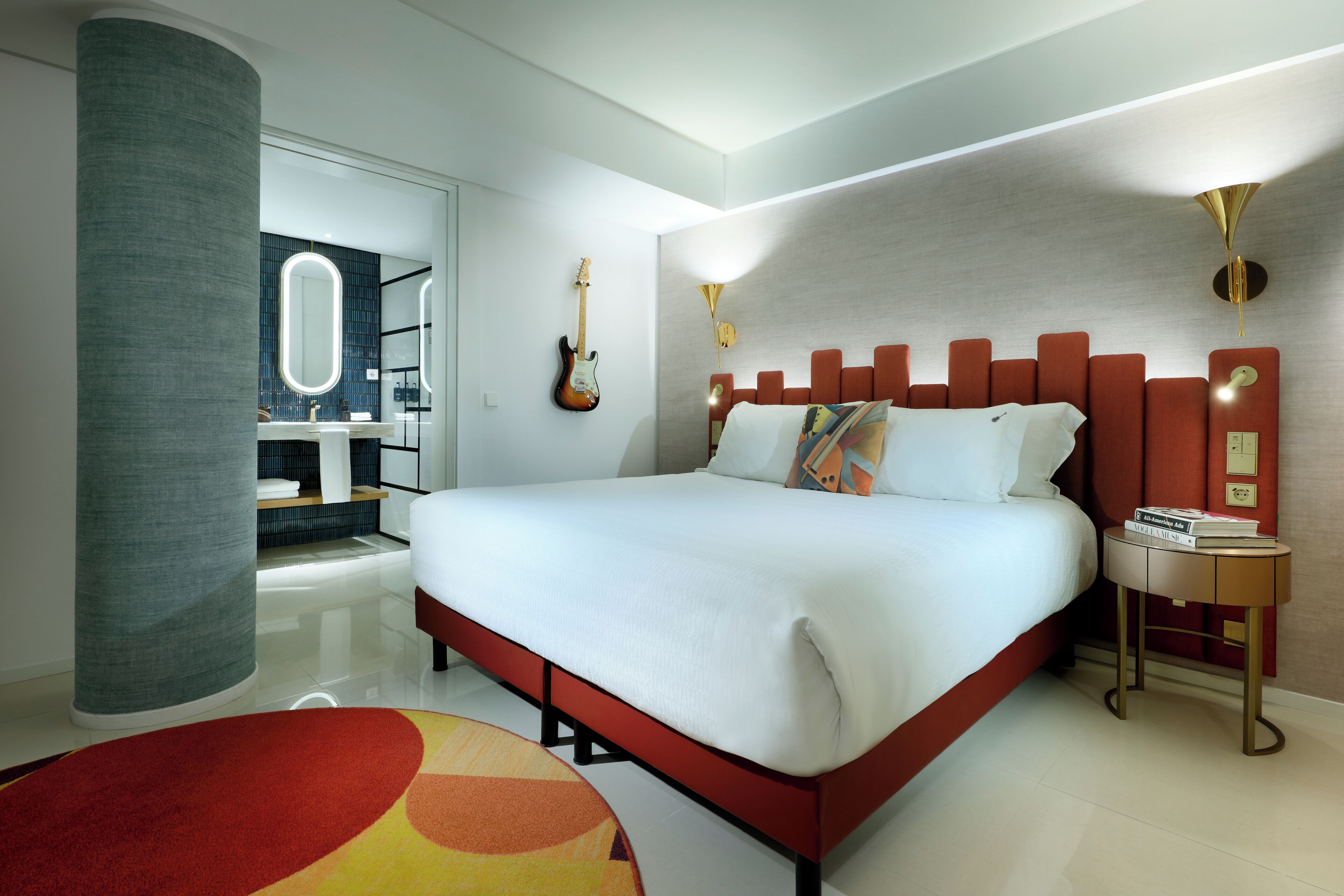 Ein modernes Hotelzimmer mit einem großen Bett, einem Badezimmer mit Spiegel und einer Gitarre an der Wand.