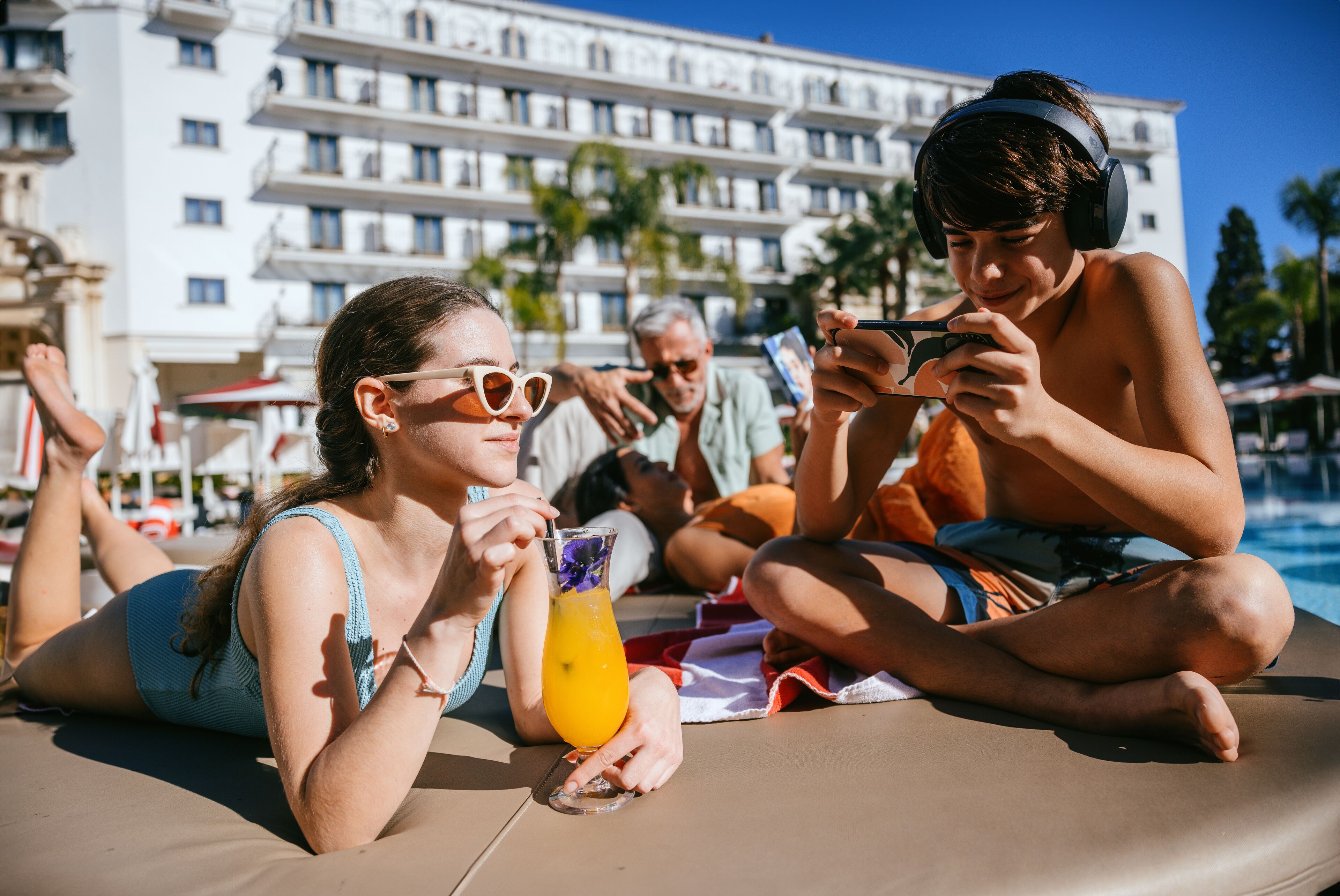 A poolside area with a lounge chair, a person holding a drink, and a building in the background.