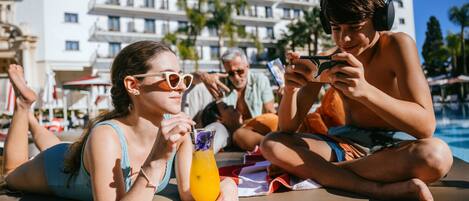 A poolside area with a lounge chair, a person holding a drink, and a building in the background.