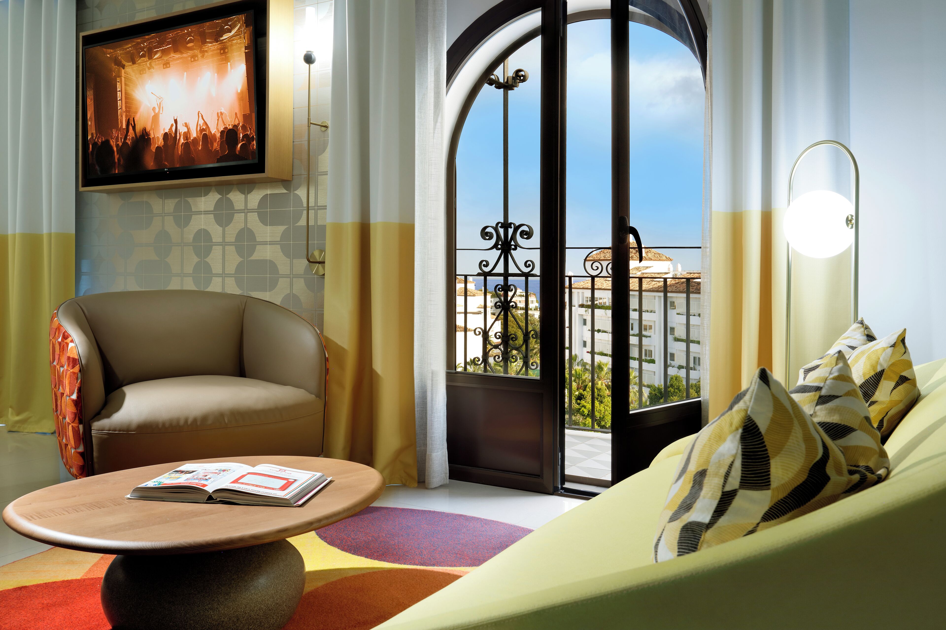 A modern hotel room with a sofa, armchair, and a table with a magazine.