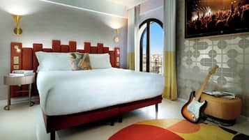 Una habitación de hotel moderna con una cama grande, un televisor y una guitarra.