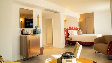 Habitación de hotel con cama, escritorio con computadora, silla y pequeña mesa con reproductor de discos.