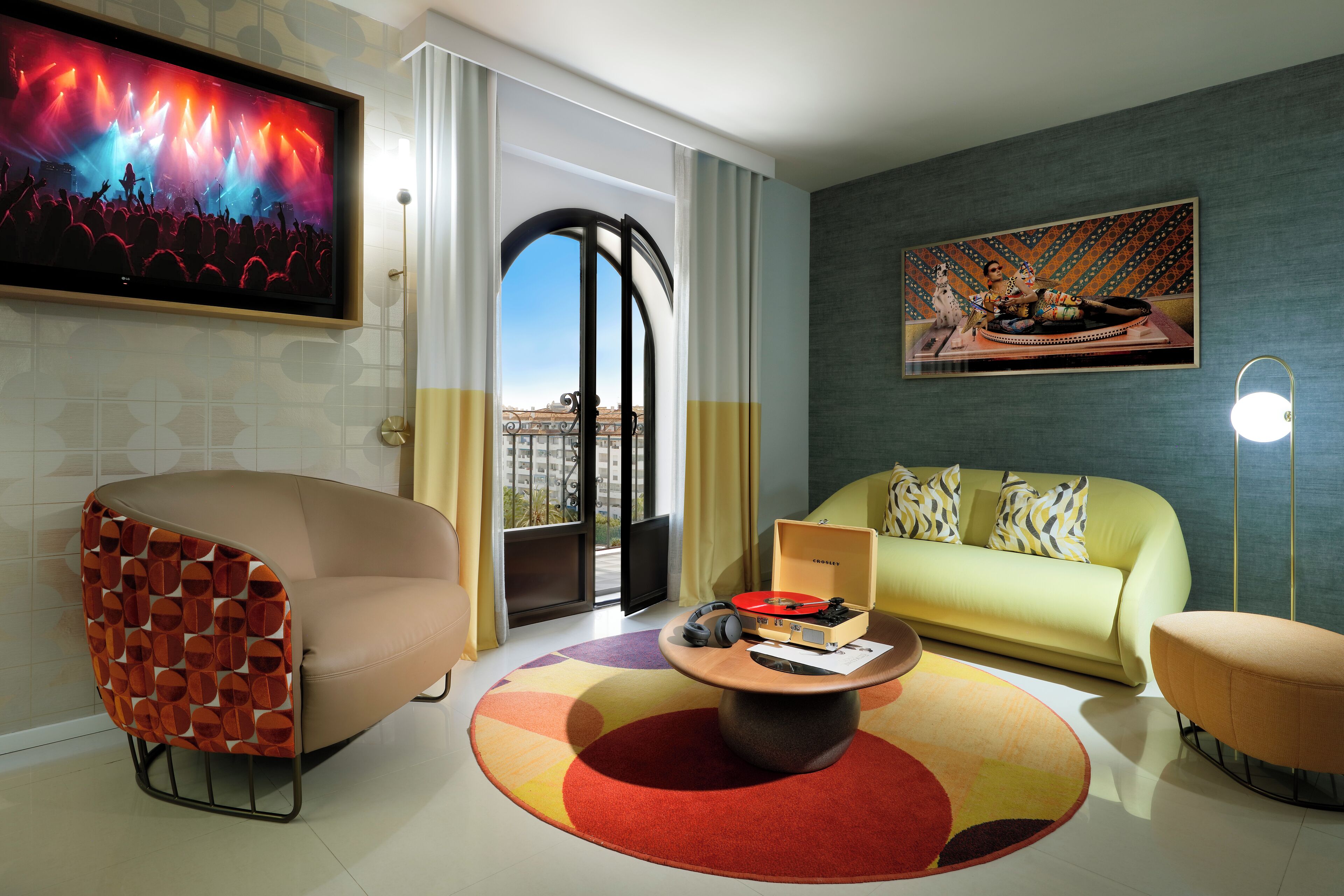 A modern living room with a sofa, a unique chair, a coffee table with a record player, and a large painting on the wall.