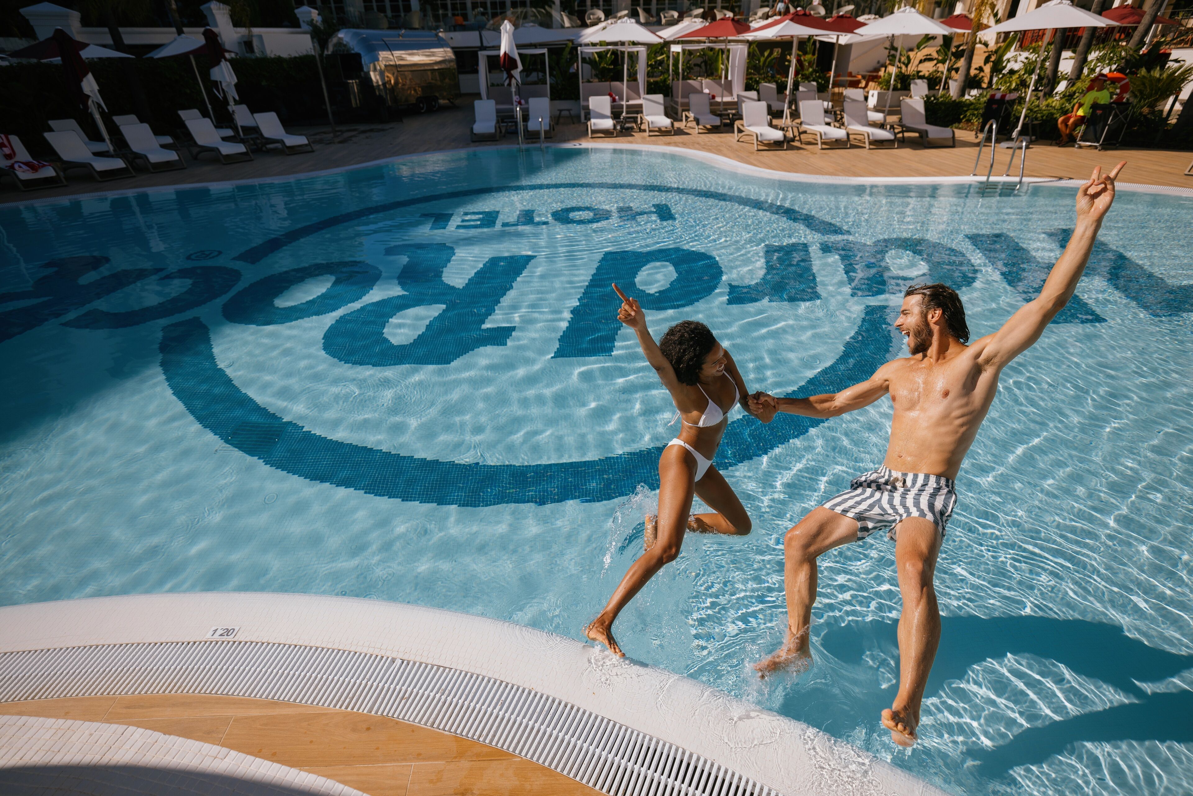 A swimming pool with a logo, lounge chairs, and umbrellas.