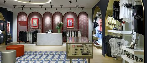 A modern retail store with a central display table, clothing racks, and a patterned carpet.