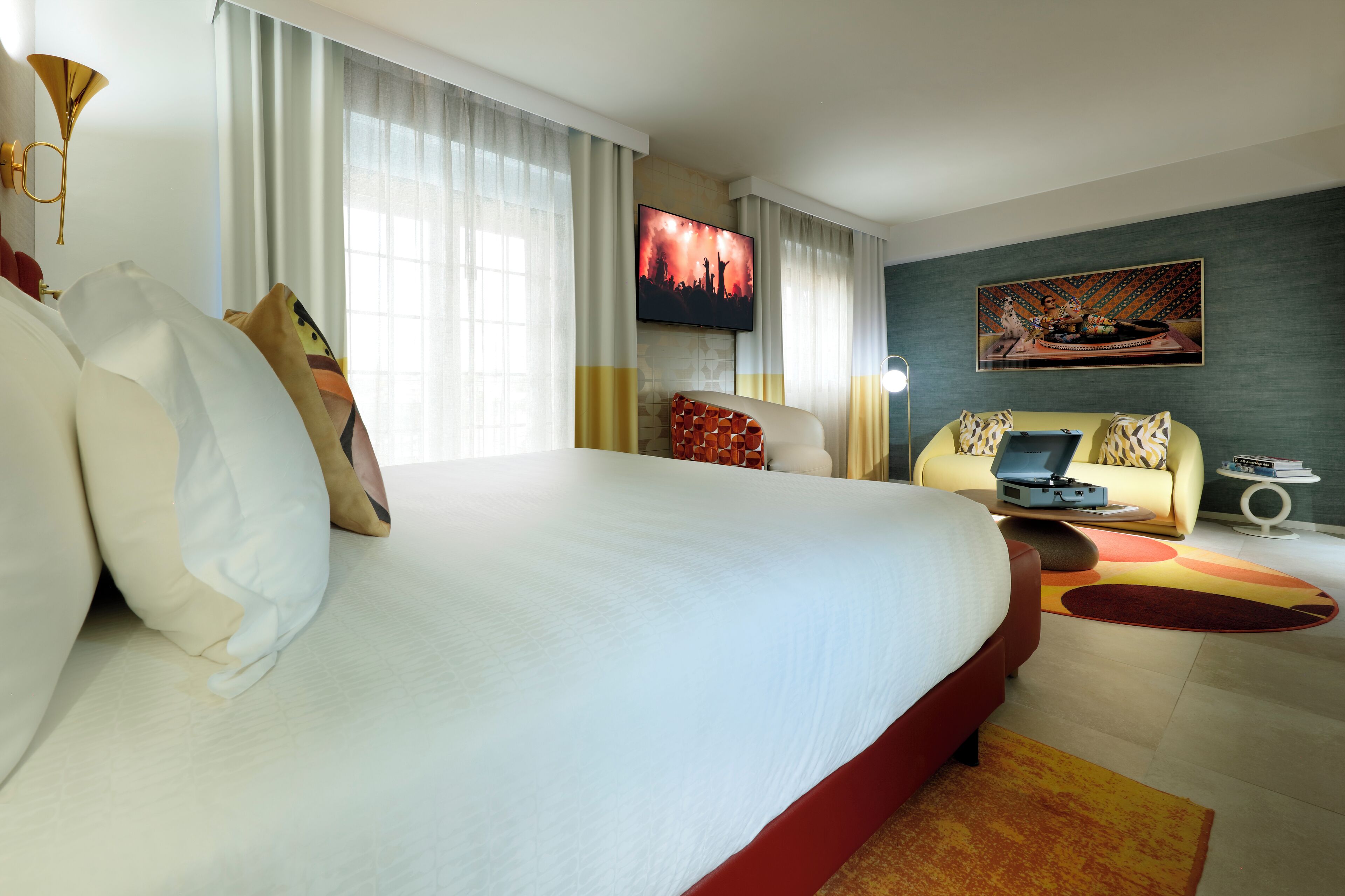 A hotel room with a large bed, a sofa, a TV, and a painting on the wall.