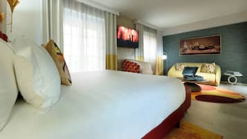 A hotel room with a large bed, a sofa, a TV, and a painting on the wall.