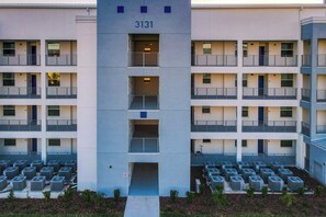 A multi-story building with numbered windows and air conditioning units on the ground level.