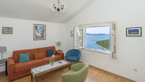 Een woonkamer met een bank, fauteuil en een salontafel. Er is een raam met uitzicht op zee.