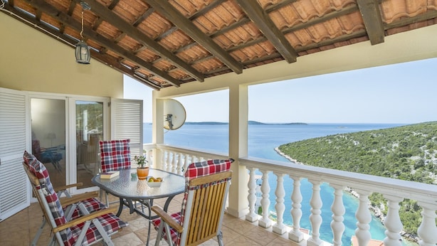 Een balkon met een tafel en stoelen, uitzicht op zee en een schotelantenne.